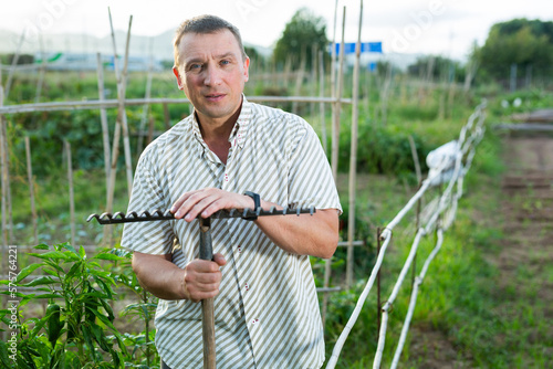 Adult man farmer with rake standing at farm outdoor photo