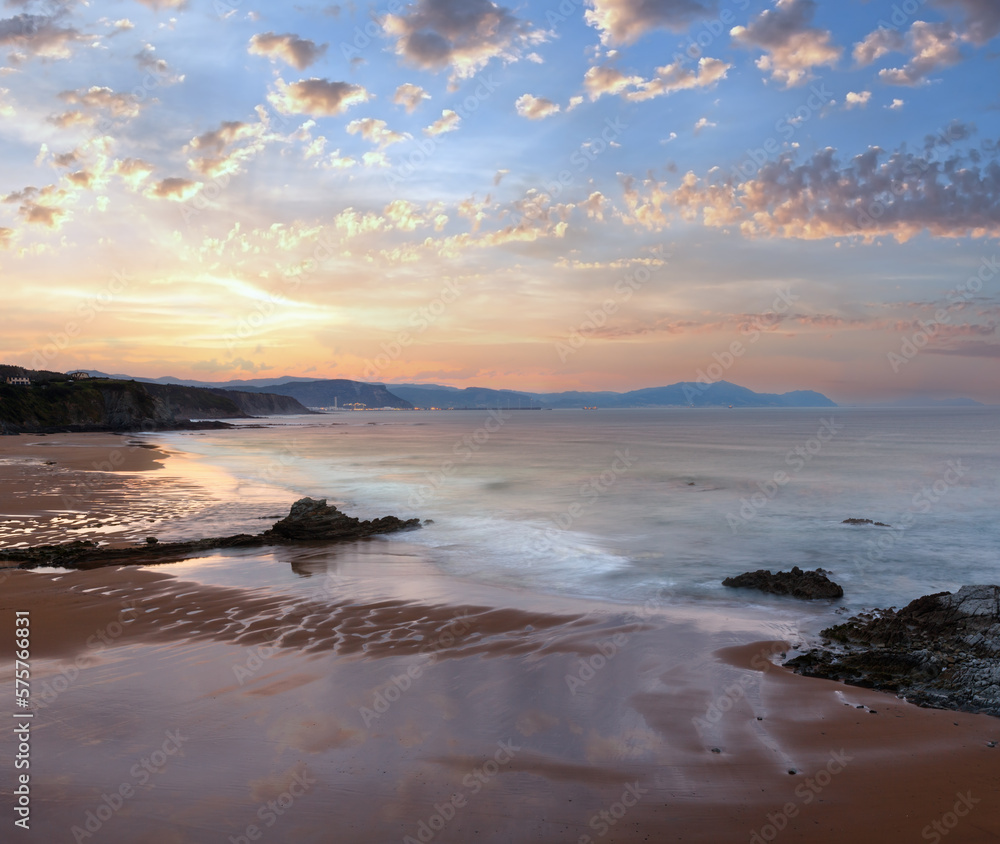 Twilight ocean rocky coast landscape with sky reflection on wet sand of beach (Spain).