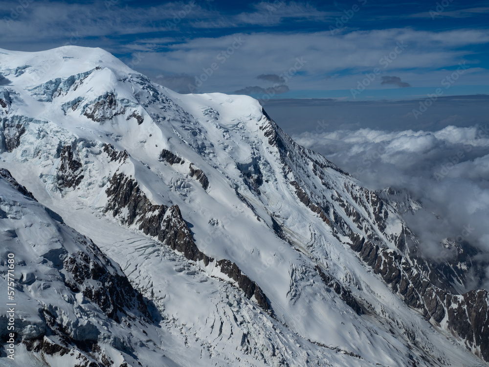 Obraz premium Majestic view of Mont Blanc near Chamonix, showcasing its snow-covered slopes, rugged peaks, and deep crevasses. Clouds hover over the valleys, adding to the breathtaking alpine scenery