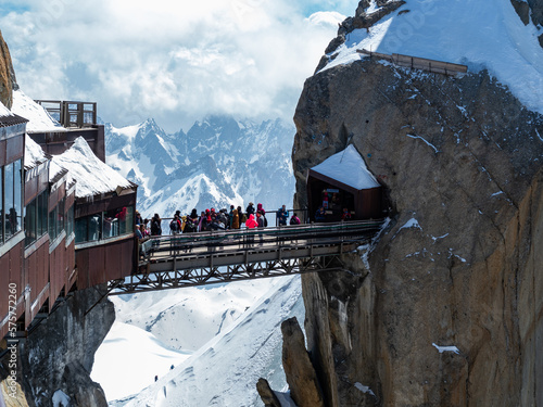 Chamonix, France Aiguille du Midi, lift station and bridge over the precipice with stunning view over white peaks of Alps. People standing on the bridge.