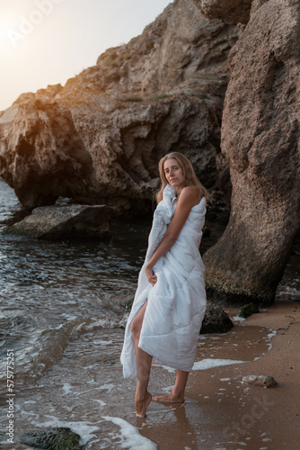 a girl in a white blanket walks along the beach at the sea, near the rocks. Beautiful, slender legs walk along the beach. Cream for varicose veins. High quality photo