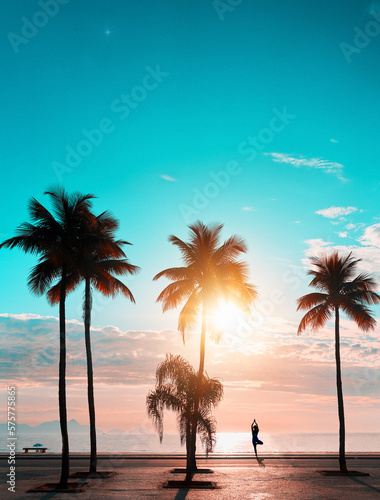 sunrise view over the atlantic ocean in Copacabana with silhouette of palm trees and a woman in yoga pose on the beach against light