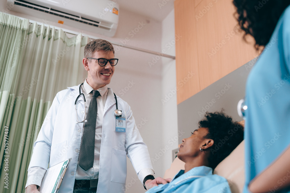 Obraz premium Handsome young experienced doctor and surgeon with eyeglasses wearing lab coat and stethoscope talking and comforting male patient with nurse after surgery in hospital