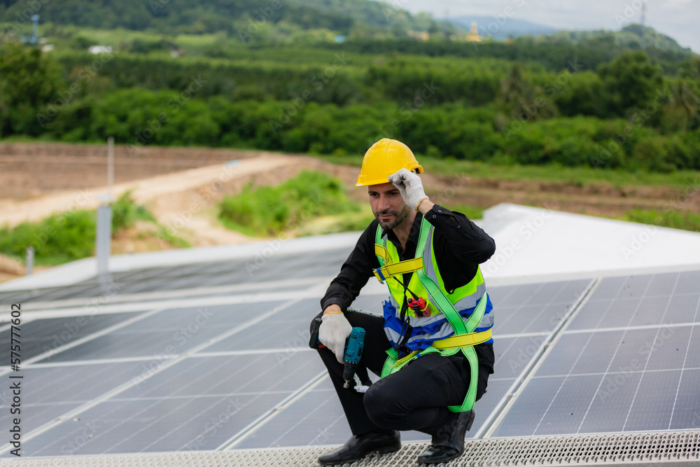 Handsome young male engineer wearing safety vest and jacket with gloves and tools along with hard hat helmet standing on solar panel while checking and looking at its maintenance Handsome young male engineer wearing safety vest and jacket with gloves and tools along with hard hat helmet standing on solar panel while checking and looking at its maintenance