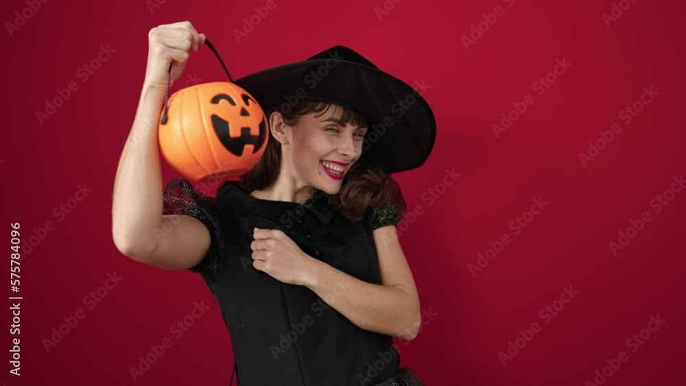 Young caucasian woman wearing witch costume covering face with halloween pumpkin basket over isolated red background Young caucasian woman wearing witch costume covering face with halloween pumpkin basket over isolated red background