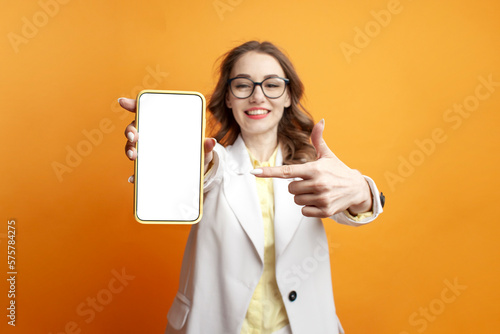Φωτογραφία business girl in glasses and suit shows blank smartphone screen on colored backg