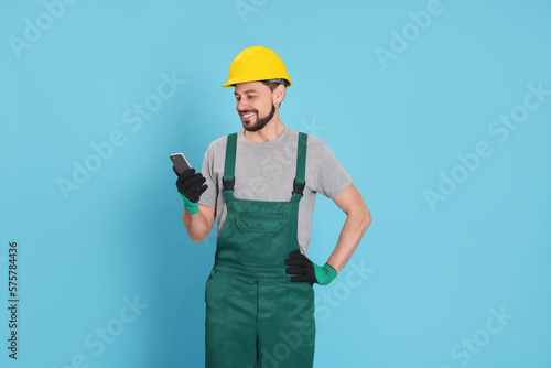 Professional repairman in uniform with phone on light blue background