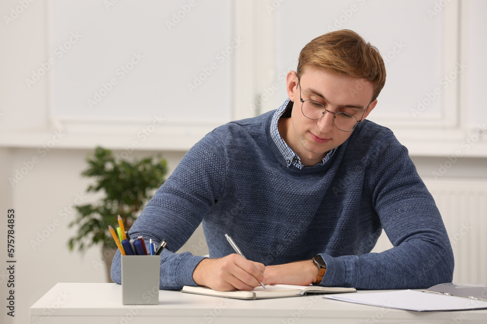 Young man writing in notebook at table indoors Young man writing in notebook at table indoors