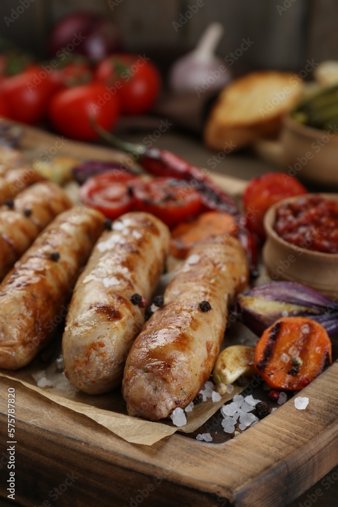Tasty grilled sausages with vegetables on wooden board, closeup