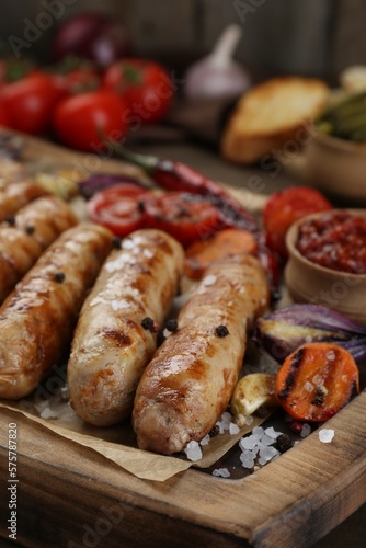 Tasty grilled sausages with vegetables on wooden board, closeup
