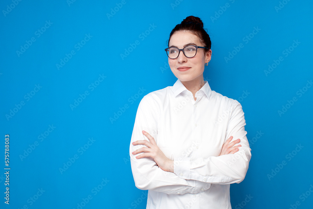 young girl office worker in white shirt and glasses stands with her arms crossed on blue background young girl office worker in white shirt and glasses stands with her arms crossed on blue background