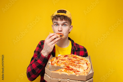 shocked guy eats pizza on yellow background and shows surprise, hungry student enjoys fast food