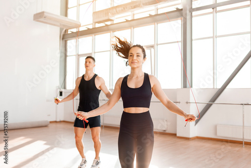 athletic couple in sportswear jumping rope in gym in morning, fitness girl and coach man go in for sports in training photo