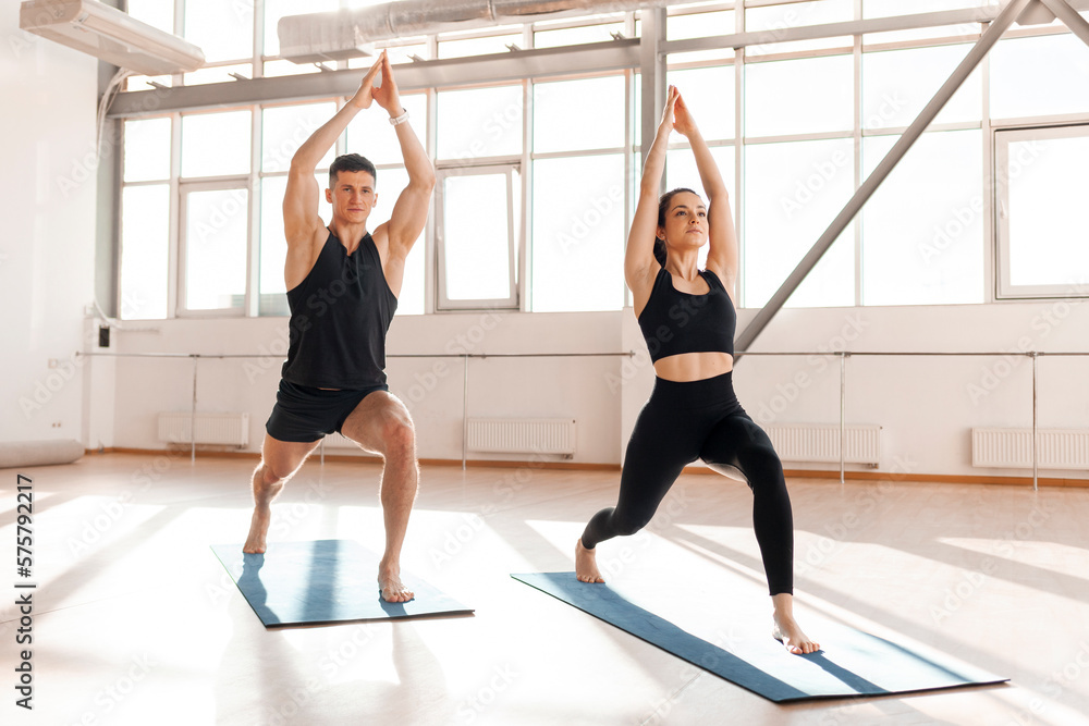 athletic couple in sportswear sit in yoga pose on yoga mats in the morning, fitness girl and trainer man meditate