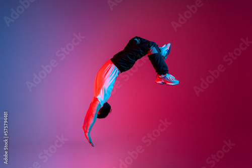 young guy falls upside down in the air, man levitates and flies down in neon lighting, acrobat dancer flies in jump