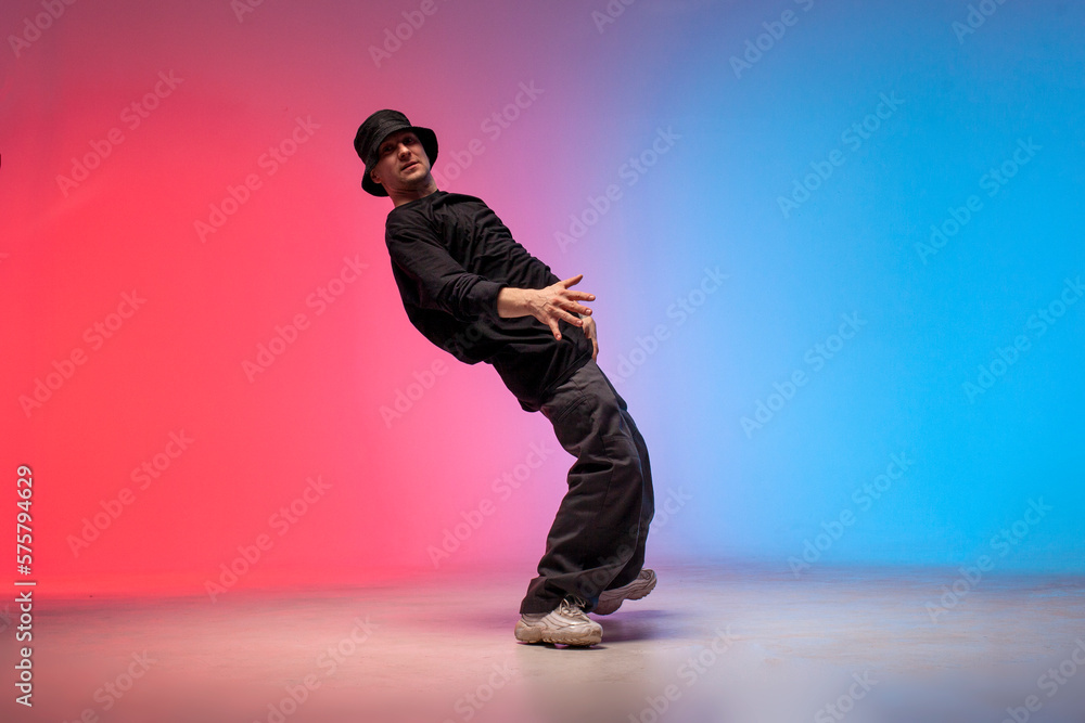 dancer dances hip hop in neon lighting, young guy moves his arms to the sides and dances break dance