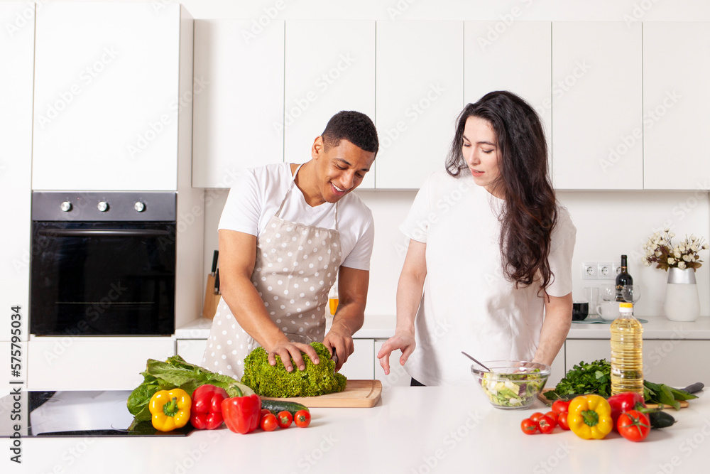 multiracial couple in kitchen preparing salad together, american guy and european girl preparing veggie food