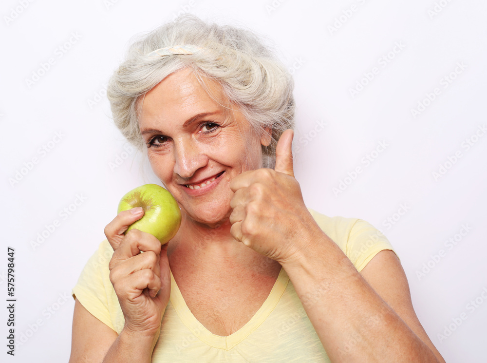 Mature smiling woman with white hair holding green apple over white background Mature smiling woman with white hair holding green apple over white background