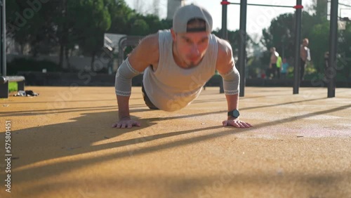 Athletic man doing push up exercises on sports ground in park. Caucasian male athlete doing press up workout training outside gym sunny summer day.