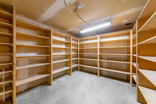 Interior view of a house pantry or walk in closet that is under construction. Unpainted wooden shelves, floor, and ceiling can also be seen inside the unfinished storage room.