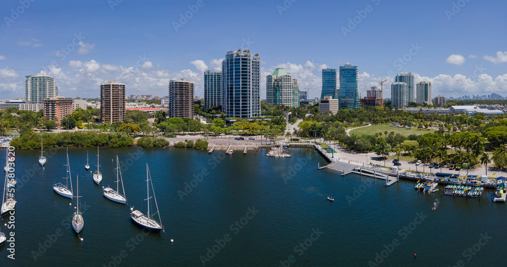 Obraz premium Dinner Key Marina and Coconut Grove Sailing Club on a sunny day in Miami Florida. Aerial view of boats anchored at sea with beautiful city skyline and blue sky in the background.