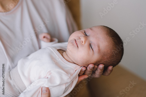 Portrait of baby sweet sleeping on mother's hands. Loving mom carying of her newborn baby at home. Mother hugging her little 1 months old girl.