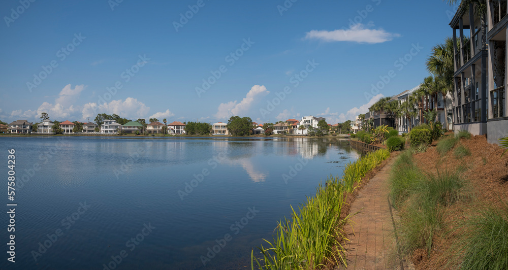 Narrow bricks pathway on the shore of Four Prong Lake in Destin, Florida. Views of houses in panorama surrounding the lake against the blue sky.