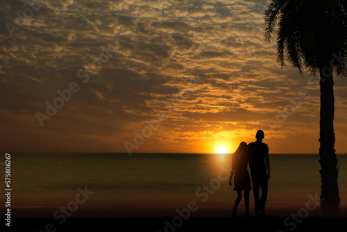 silhouette of a couple standing on the beach in the morning sun rising in the sea © Warawut