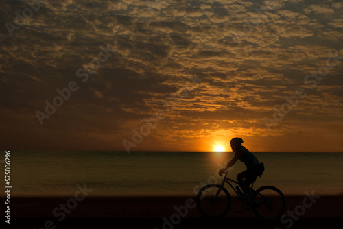 A silhouette of a cyclist riding on a beach road in the setting sun rising in the morning.