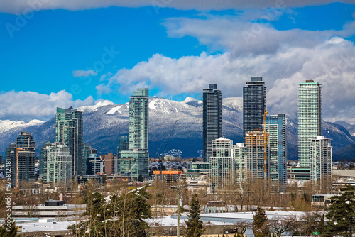 New residential area of high-rise buildings in the city of Burnaby, construction site in the center of the city against the backdrop of snow covered mountain range and blue cloudy sky