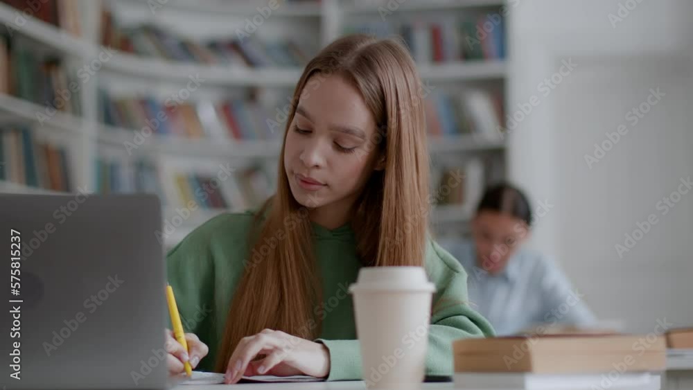 Education process. Young concentrated woman student writing notes at copybook, studying with classmates at classroom Education process. Young concentrated woman student writing notes at copybook, studying with classmates at classroom