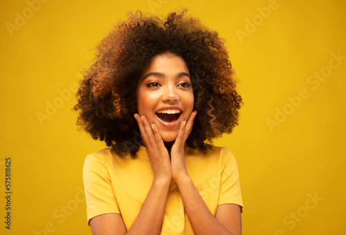 Young African Woman Surprised Smiling at Camera on Yellow Background.