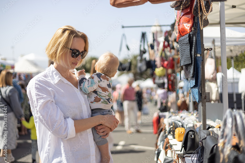 Fototapeta premium Mother hoding his infant baby boy child whilechecing items at sunday flea market