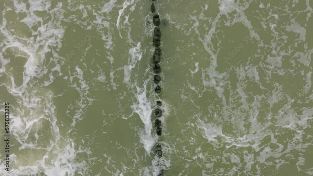Aerial birdseye view of Baltic sea coast on a overcast day, old wooden pier, white sand beach, large storm waves crushing against the coast, climate changes, wide ascending drone shot Aerial birdseye view of Baltic sea coast on a overcast day, old wooden pier, white sand beach, large storm waves crushing against the coast, climate changes, wide ascending drone shot