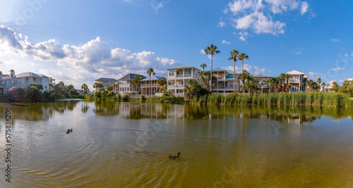 Destin, Florida- Freshwater lake with ducks at the front of houses. Lake panorama with tall grasses on shore near the three-storey homes against the sunny sky with clouds background.