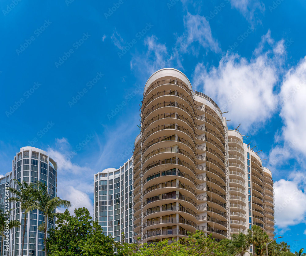 Miami Beach, Florida- Views of apartments with modern architectural structures against the sky. There are trees below the modern multi-storey apartments in a low angle view.