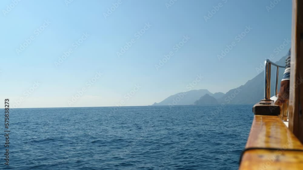 View of a man leaning against the railing of a ship sailing on the sea. In the background are the deep blue sea, high mountains and the sky. A walk on the sea. slow motion View of a man leaning against the railing of a ship sailing on the sea. In the background are the deep blue sea, high mountains and the sky. A walk on the sea. slow motion