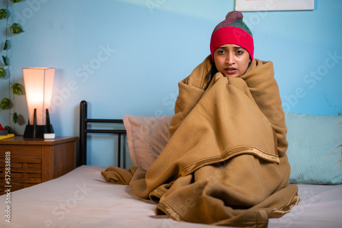 Foto shivering Young girl full coverd with blanket and cap sitting on bed at during n