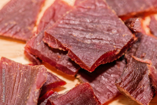 Small cuts of processes beef jerky on wooden background. 