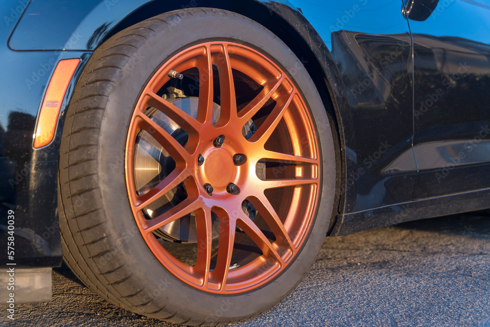 Close-up of a car wheel with metallic orange rim at Destin, Florida outdoors. Wheel of a black vehicle parked on the concrete ground.
