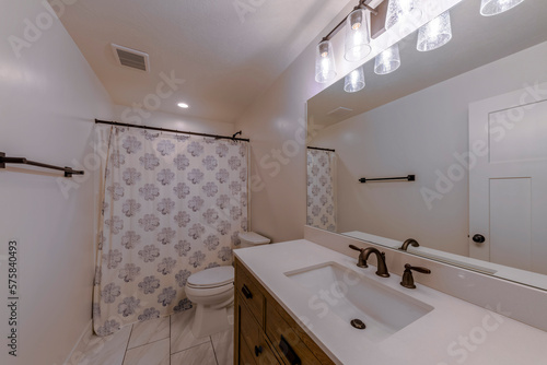 White bathroom interior with bronze faucet  curtain rod  and towel bar holder fixtures. Bathroom with marble floor tiles and rectangular sink beside the toilet near the shower curtain with floral