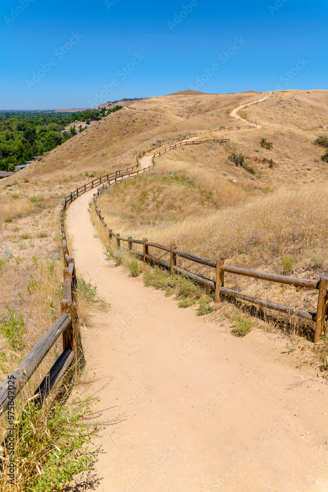 Flattened dirt path with wooden barriers on the side on a mountain at Boise, Idaho. Mountain trail in the middle of grassland against the clear blue sky background.