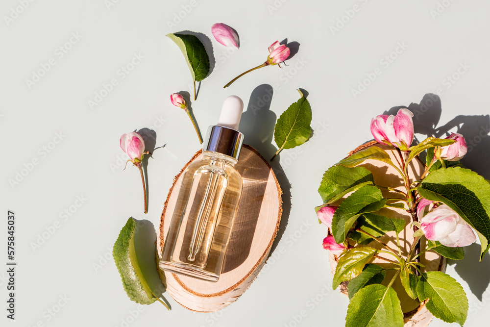 Fototapeta premium a transparent cosmetic bottle with a natural face and body care product lies on a wooden tree slice among the spring flowers of an apple tree.