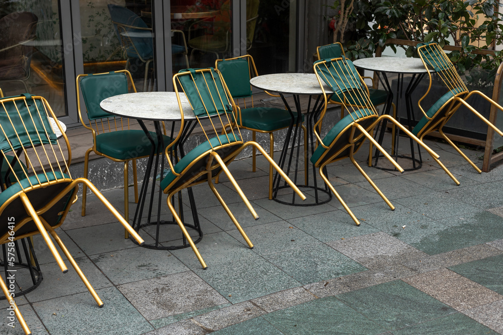 Chairs and tables in outdoor cafe. Golden chairs with green seats.