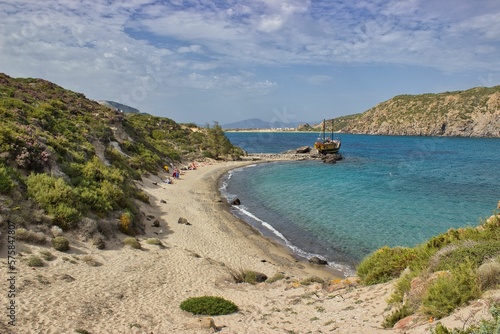 Idyllic panoramic view of a beach bay in Cyprus. The turquoise blue bay is surrounded by beach and boats, a wooden boat can be seen on the sea.
