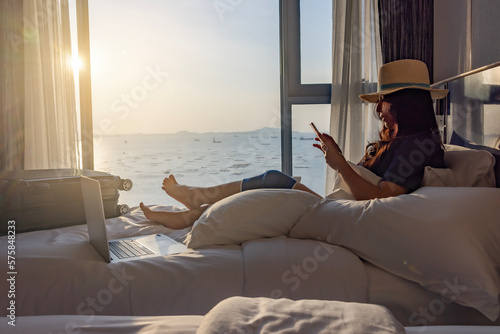 Travel insurance covers accident and medical expenses. Woman traveler with knee wrapped in medical bandage after travel accident sitting on bed in room, using smartphone and laptop to insurance online