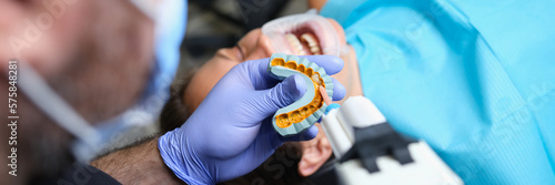 Dentist holds cast with veneers on plaster model and patient in dental clinic photo
