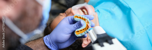 Bild auf Leinwand Dentist holds cast with veneers on plaster model and patient in dental clinic