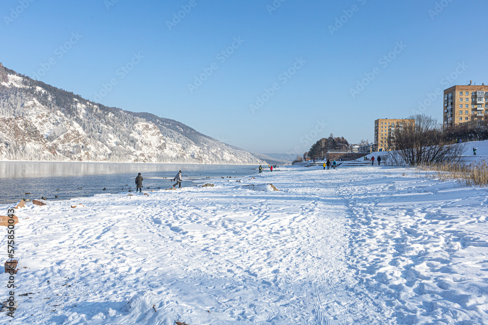 People walking along the bank of the mountain river, lake. Winter urban activities, Beautiful view of winter with crystal clear river on a cold sunny day