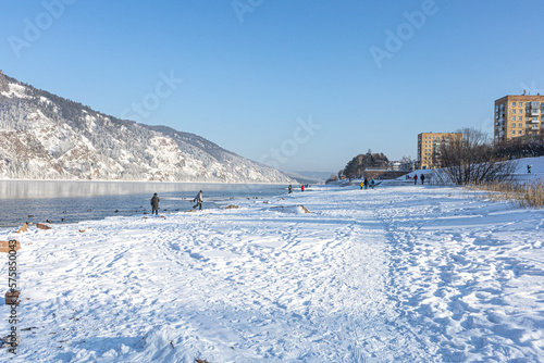 People walking along the bank of the mountain river, lake. Winter urban activities, Beautiful view of winter with crystal clear river on a cold sunny day © Anna